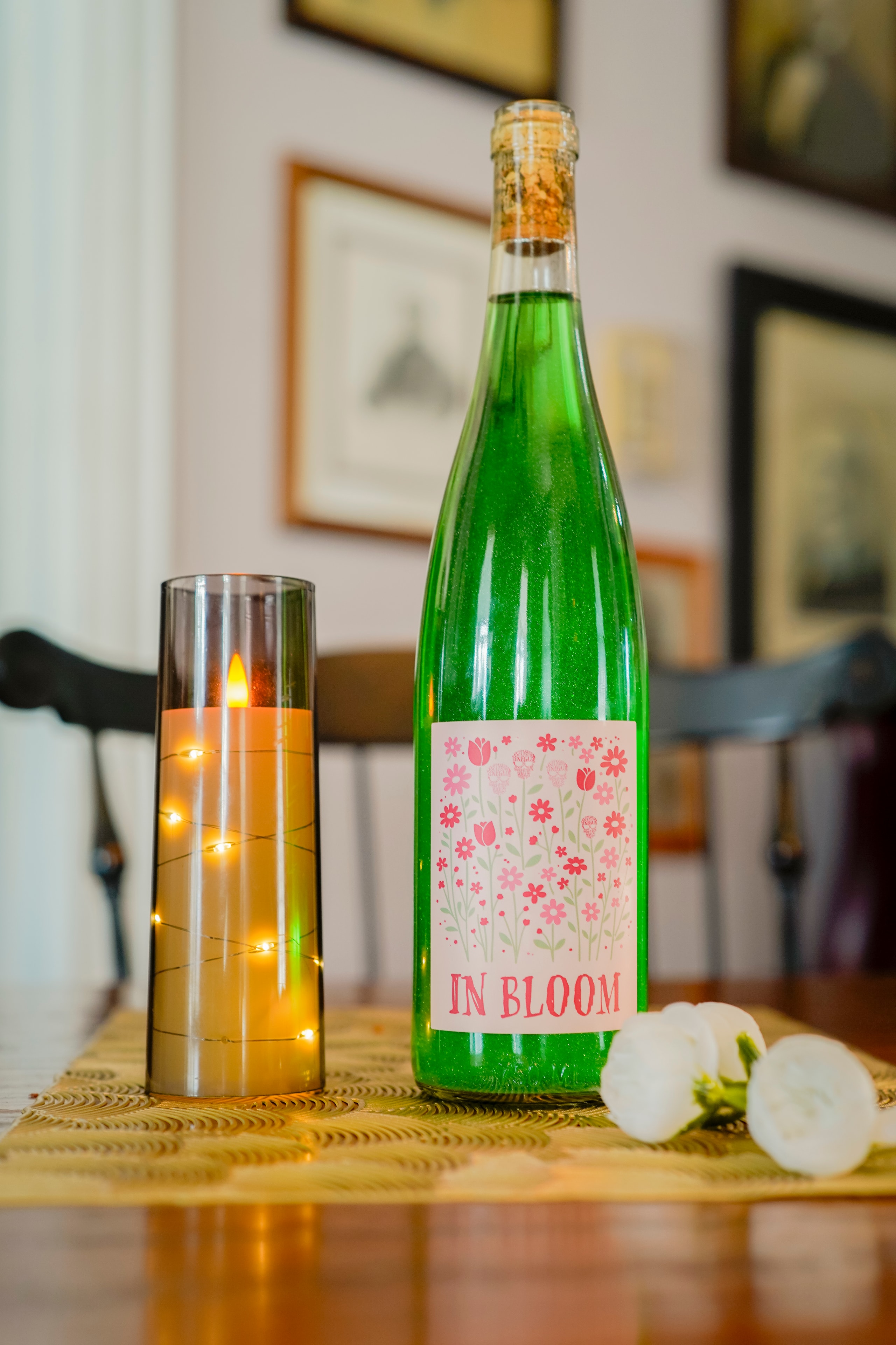 In Bloom green wine bottle with candle and white flowers on table